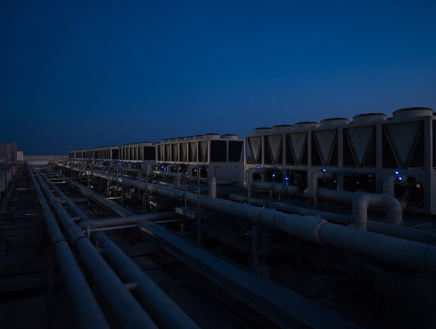 Rooftop mechanical yard with rows of chillers and chilled water pipes at dusk